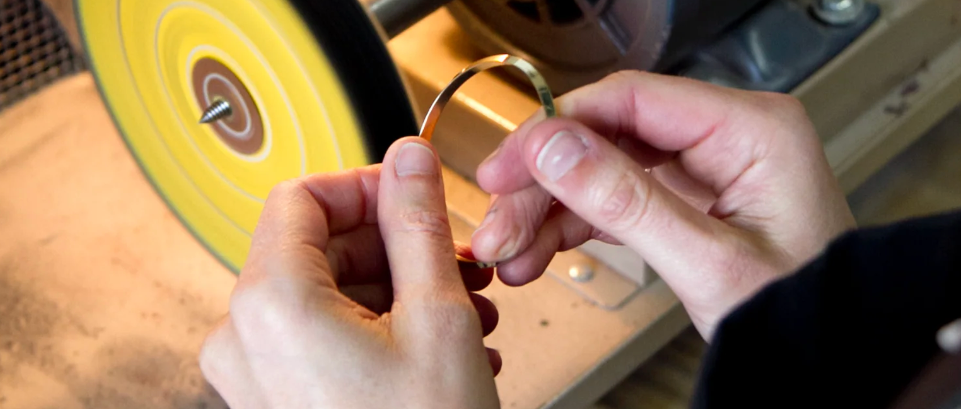 Person holding a small object near a grinding machine with a yellow wheel.