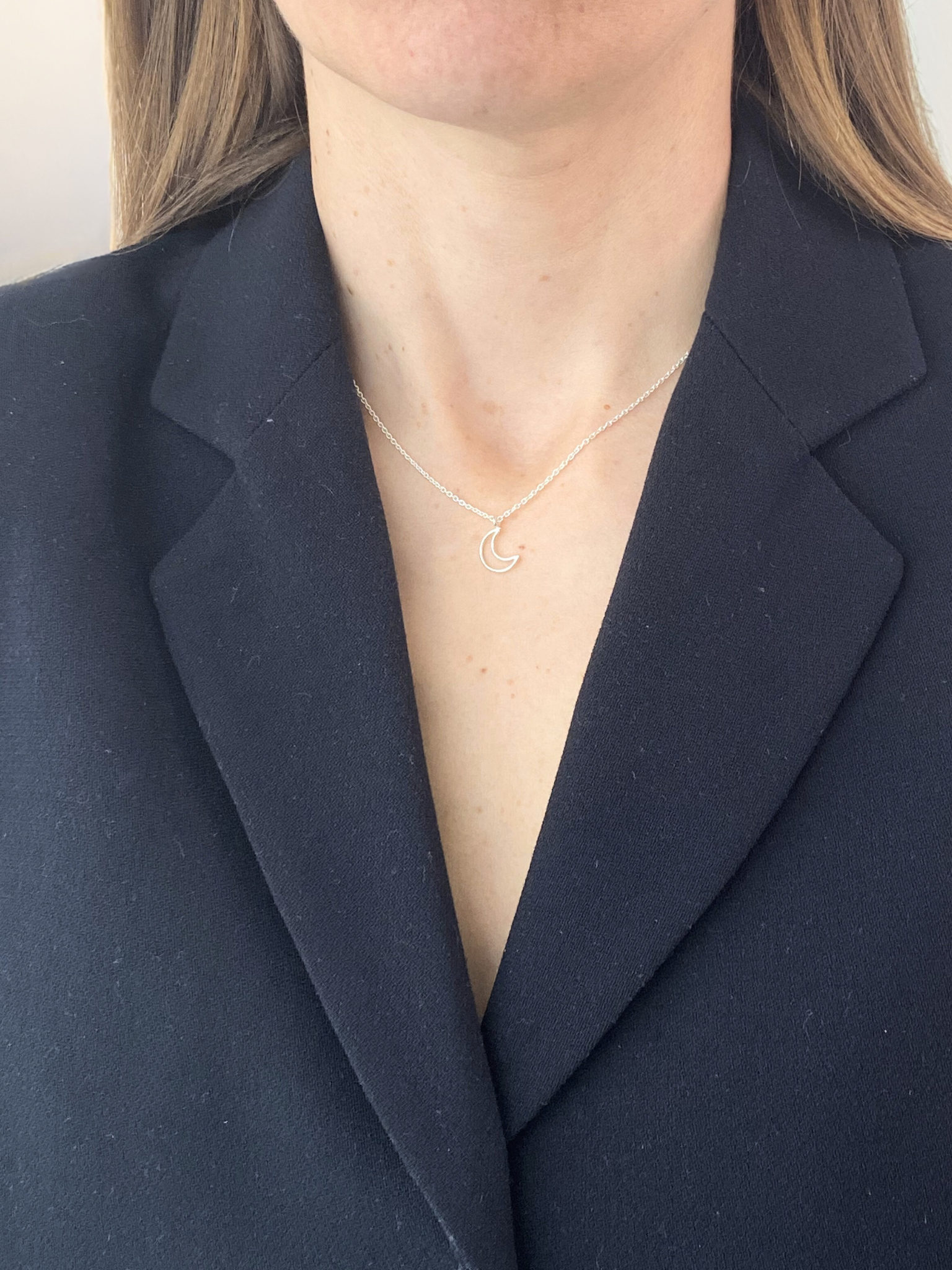 Person wearing a gold necklace with a moon pendant against a navy blazer background