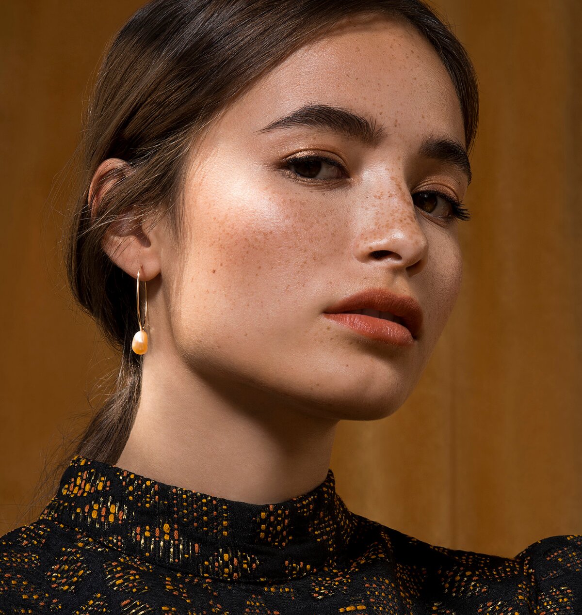 Femme qui porte une boucle d'oreilles anneau en or avec une perle d'eau douce baroque couleur pêche