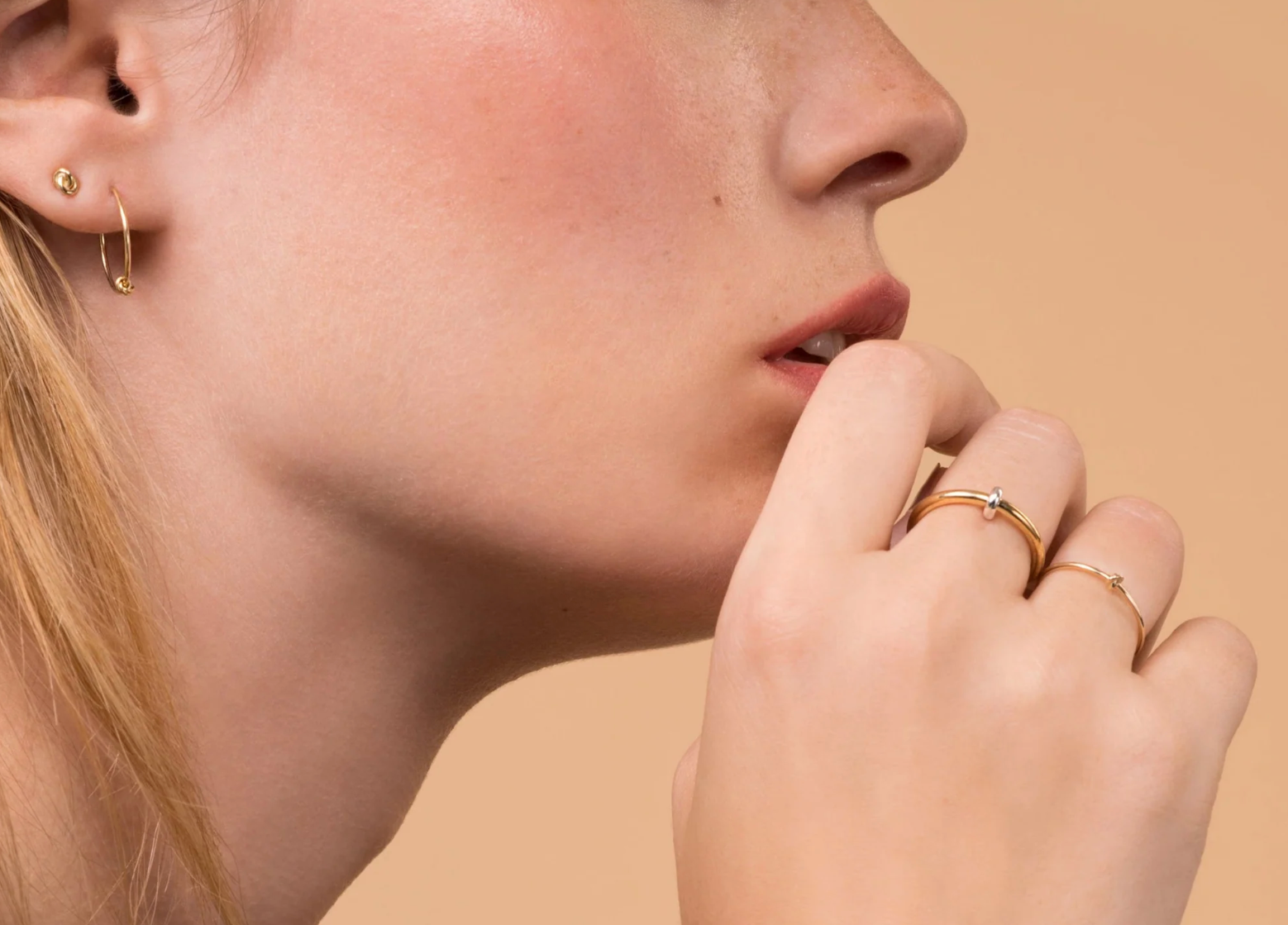 Close-up of a person wearing gold earrings and rings on a beige background