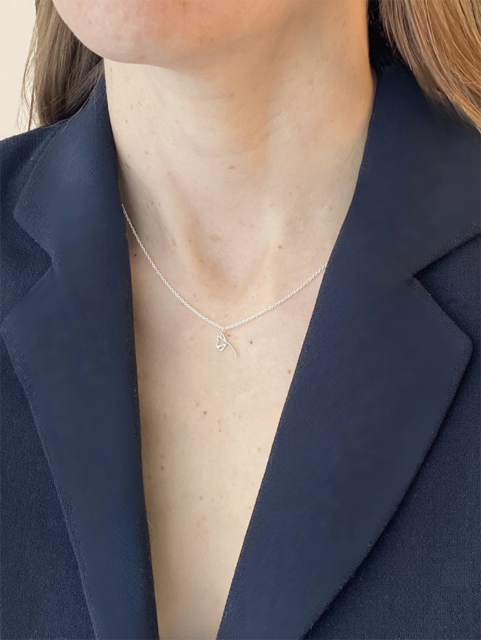 Person wearing a silver necklace with a heart pendant against a navy blazer background