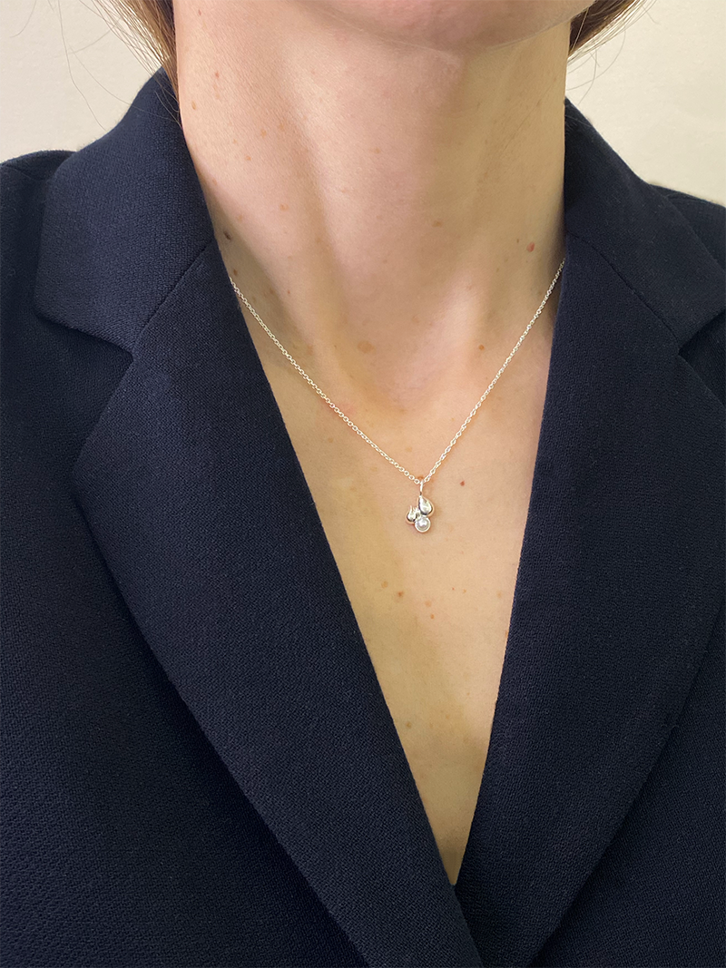Person wearing a navy blazer with a necklace featuring a small pendant.